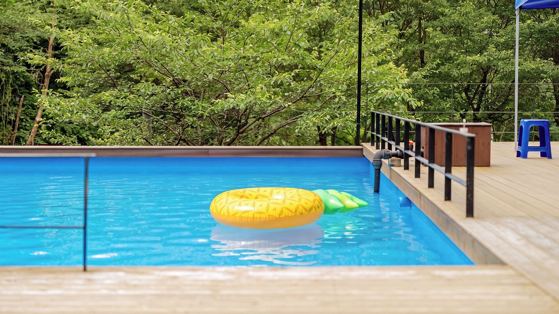 A swimming pool with a wooden deck, a blue chair, and a yellow and green inflatable float.