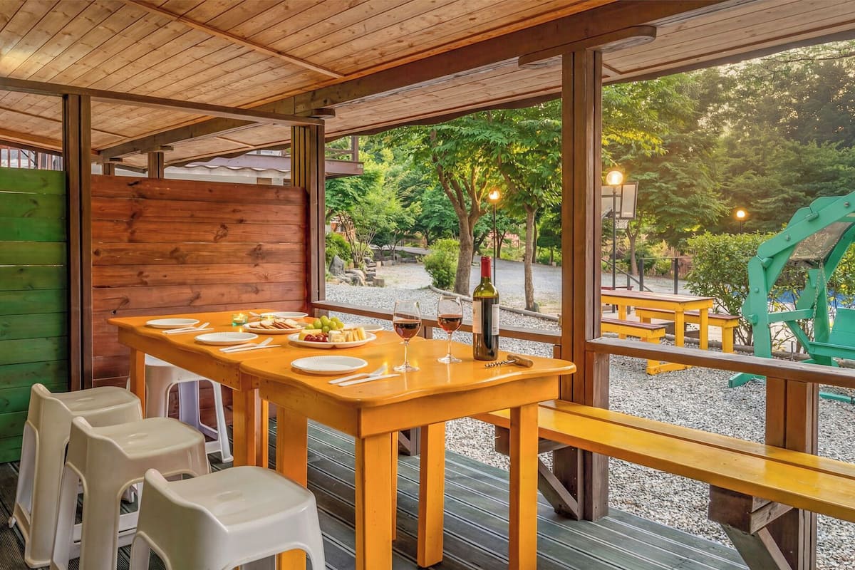 A wooden dining area with a table set for two, a bench, and a view of a garden.