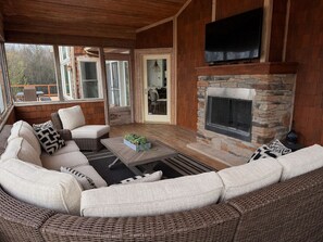 A cozy living room with a stone fireplace, wicker furniture, and a flat-screen TV mounted above the fireplace.