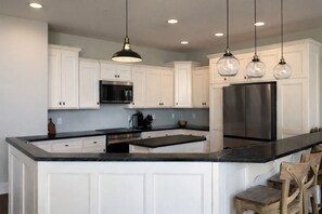 A kitchen with white cabinets, a stainless steel refrigerator, a black countertop, and pendant lights.
