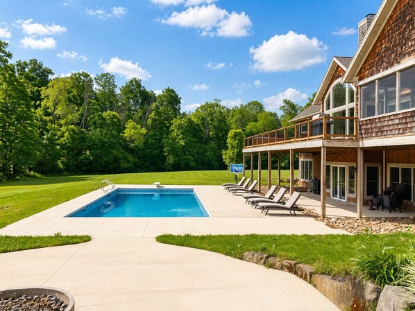 A pool with lounge chairs, a covered deck, and a house with large windows.