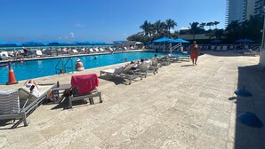 A poolside area with lounge chairs, umbrellas, and a clear blue sky. - Hotel Sunny Isles (Sunny Isles Beach)