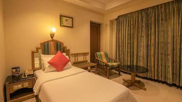 A hotel room with a bed, a chair, a small table, a nightstand, a lamp, a framed picture, and a curtain.