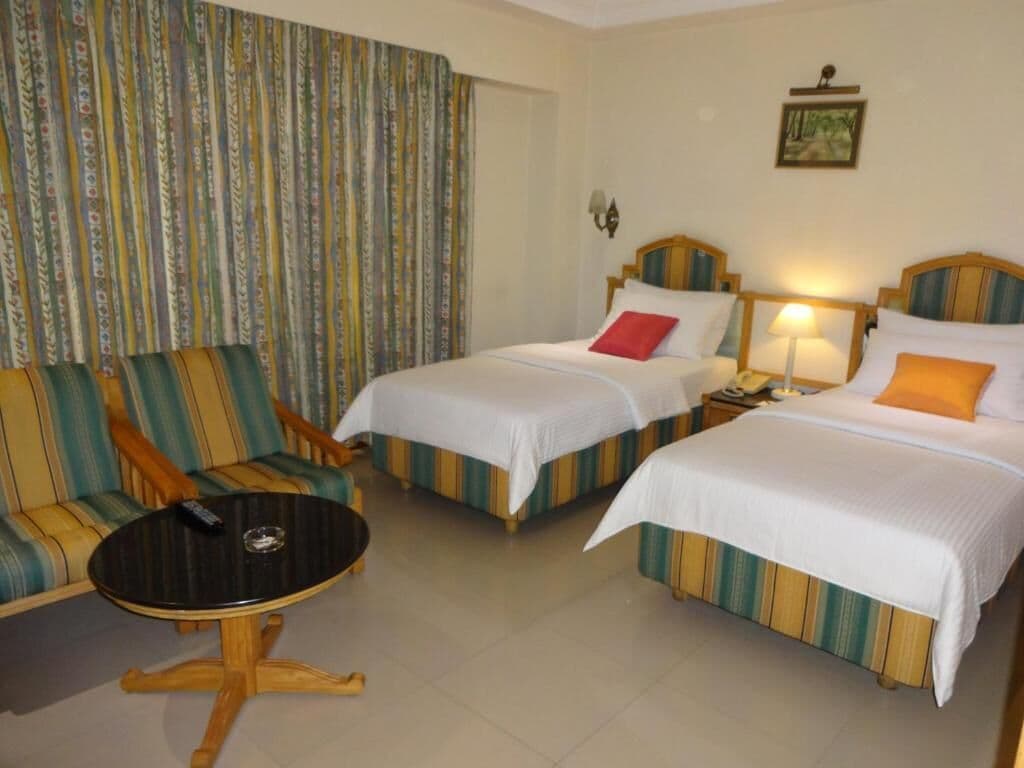 Una habitación de hotel con dos camas individuales, un sofá, una mesita y una lámpara fijada a la pared.