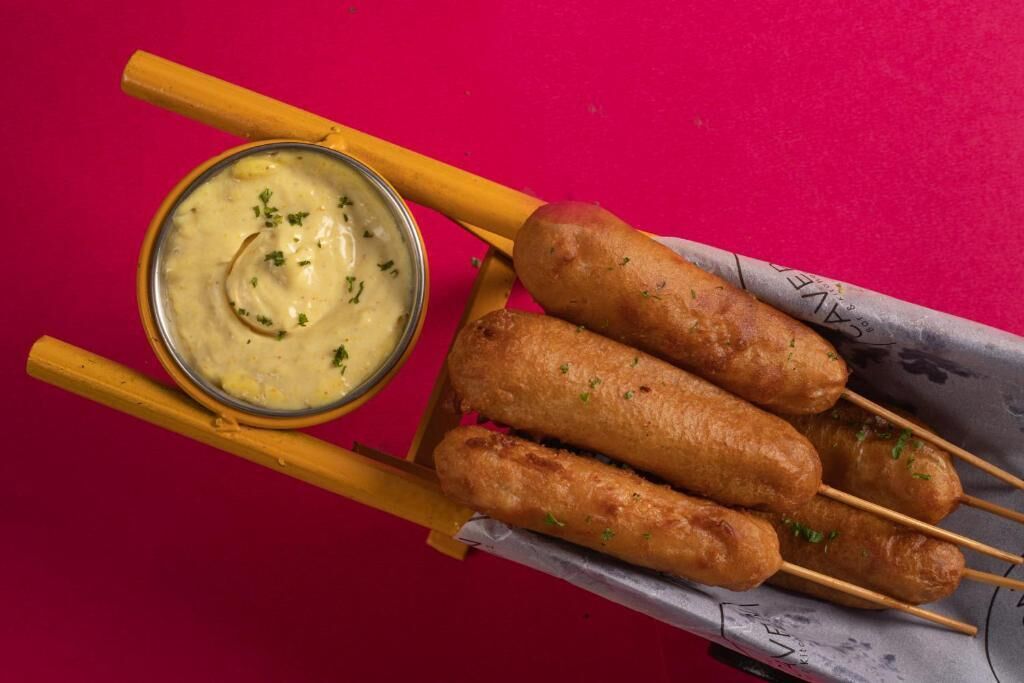 Cuatro perros calientes en brochetas con salsa para mojar en un tazón pequeño.