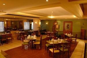 Un restaurante con mesas y sillas de madera, una zona de bar y una pared de ladrillo verde.