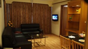 Un soggiorno con un divano nero, un tavolino in vetro, un tavolo da pranzo in legno con sedie, un televisore e un mobile in legno con una pianta.