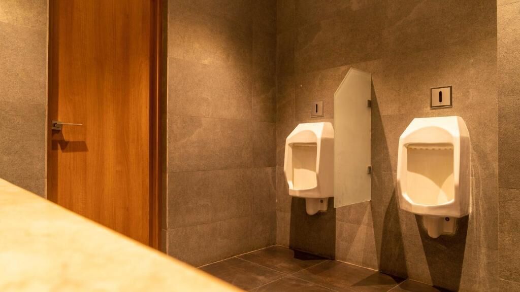 A men's restroom with two urinals, a wooden door, and a tiled floor.