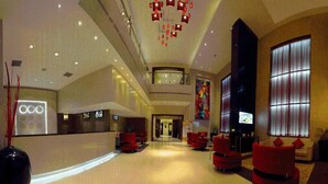 Un'ampia hall con soffitto alto, sedute rosse, una reception e un'ampia finestra con tende.