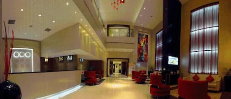 A spacious lobby with a high ceiling, red seating, a reception desk, and a large window with curtains.