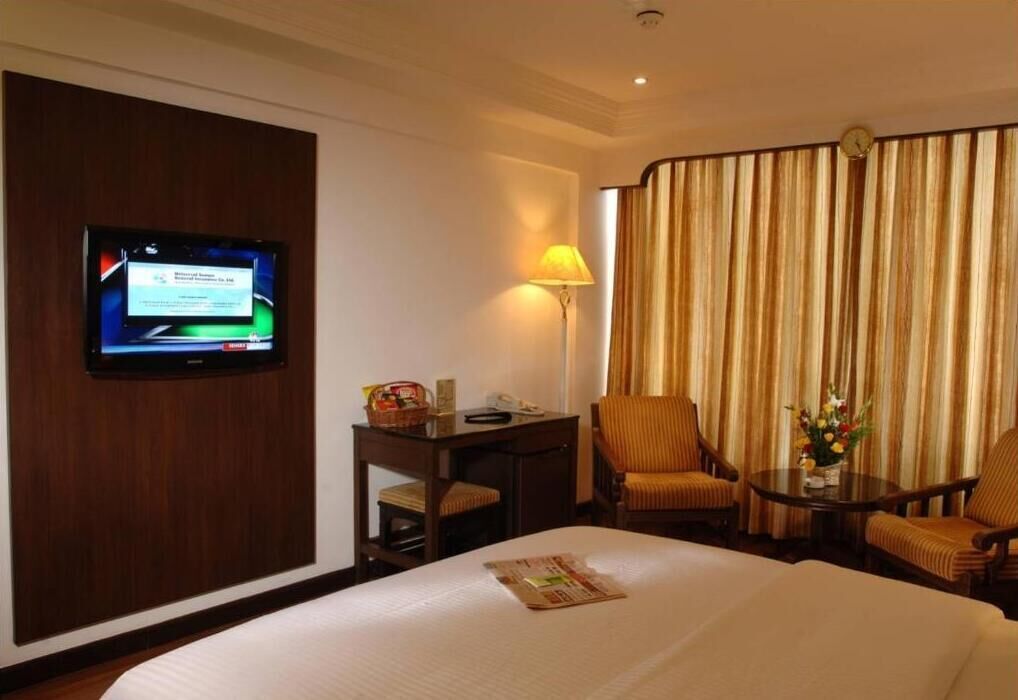 Una habitación de hotel con cama, escritorio con lámpara, televisor y vista a las cortinas.