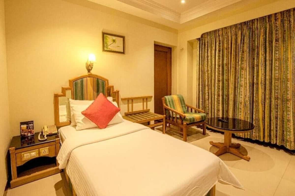 A hotel room with a bed, a chair, a small table, and a curtain.