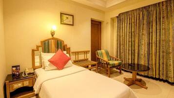Una habitación de hotel con cama, una silla, una mesita y una cortina.