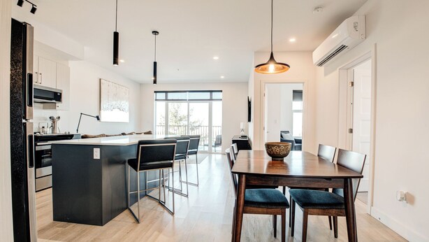 Een moderne keuken met een centraal eiland, barkrukken en een eettafel met stoelen.