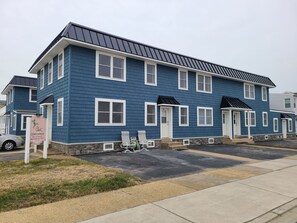 A multi-story blue building with white trim, a signboard, and a parking area. - Beautiful 1-bedroom condo across the street from the beach w/ AC (Brigantine)
