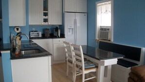 A compact kitchen with white cabinets, a refrigerator, a microwave, and a dining table with chairs. - Beautiful 1-bedroom condo across the street from the beach w/ AC (Brigantine)