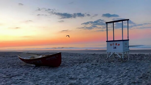 A beach with a lifeguard tower labeled 'LGBA 34' and a red boat. - Beautiful 1-bedroom condo across the street from the beach w/ AC (Brigantine)