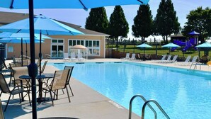 Piscina com espreguiçadeiras e guarda-sóis, área de estar coberta e parque infantil cercado.