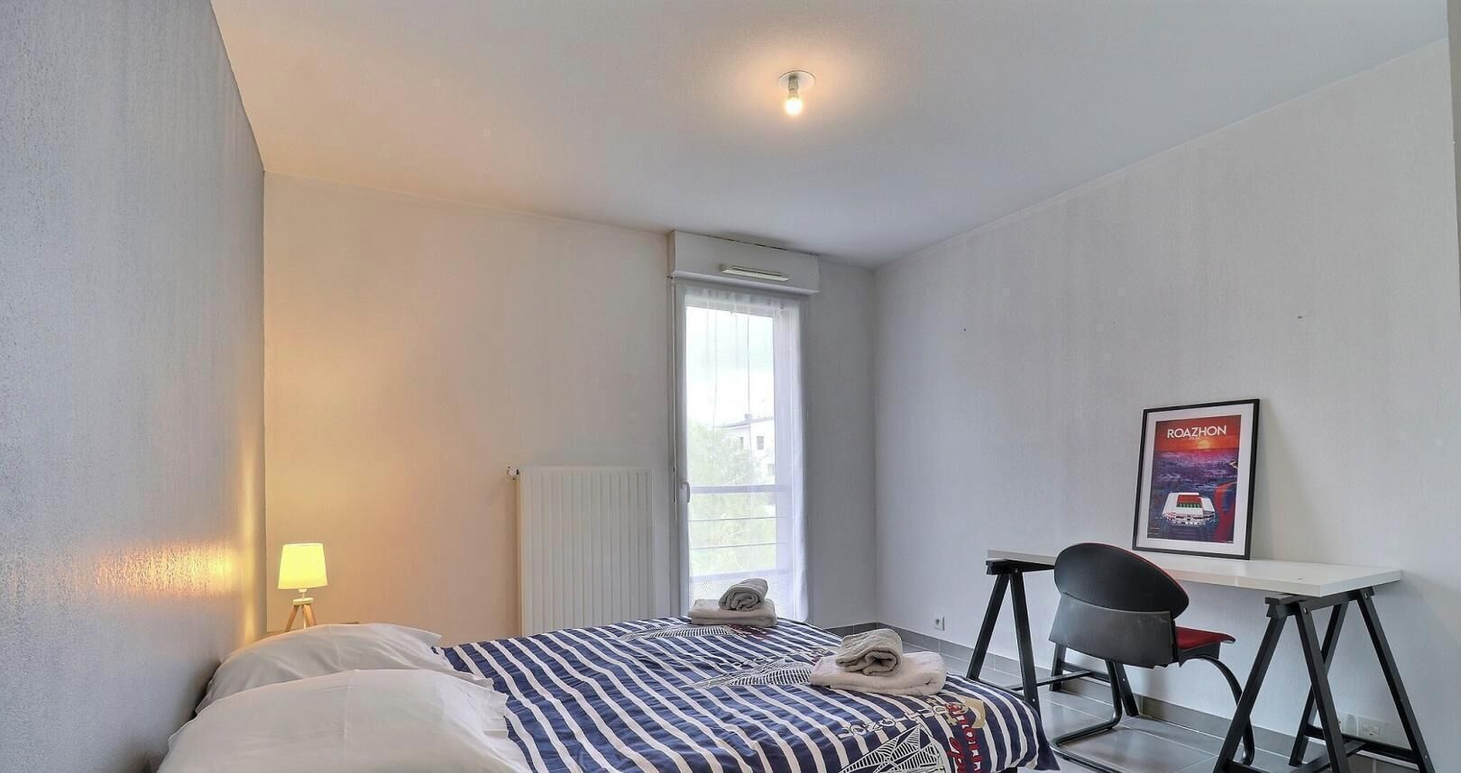 A bedroom with a bed, a desk, a chair, a radiator, and a window.