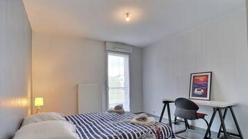 A bedroom with a bed, a desk, a chair, a radiator, and a window.