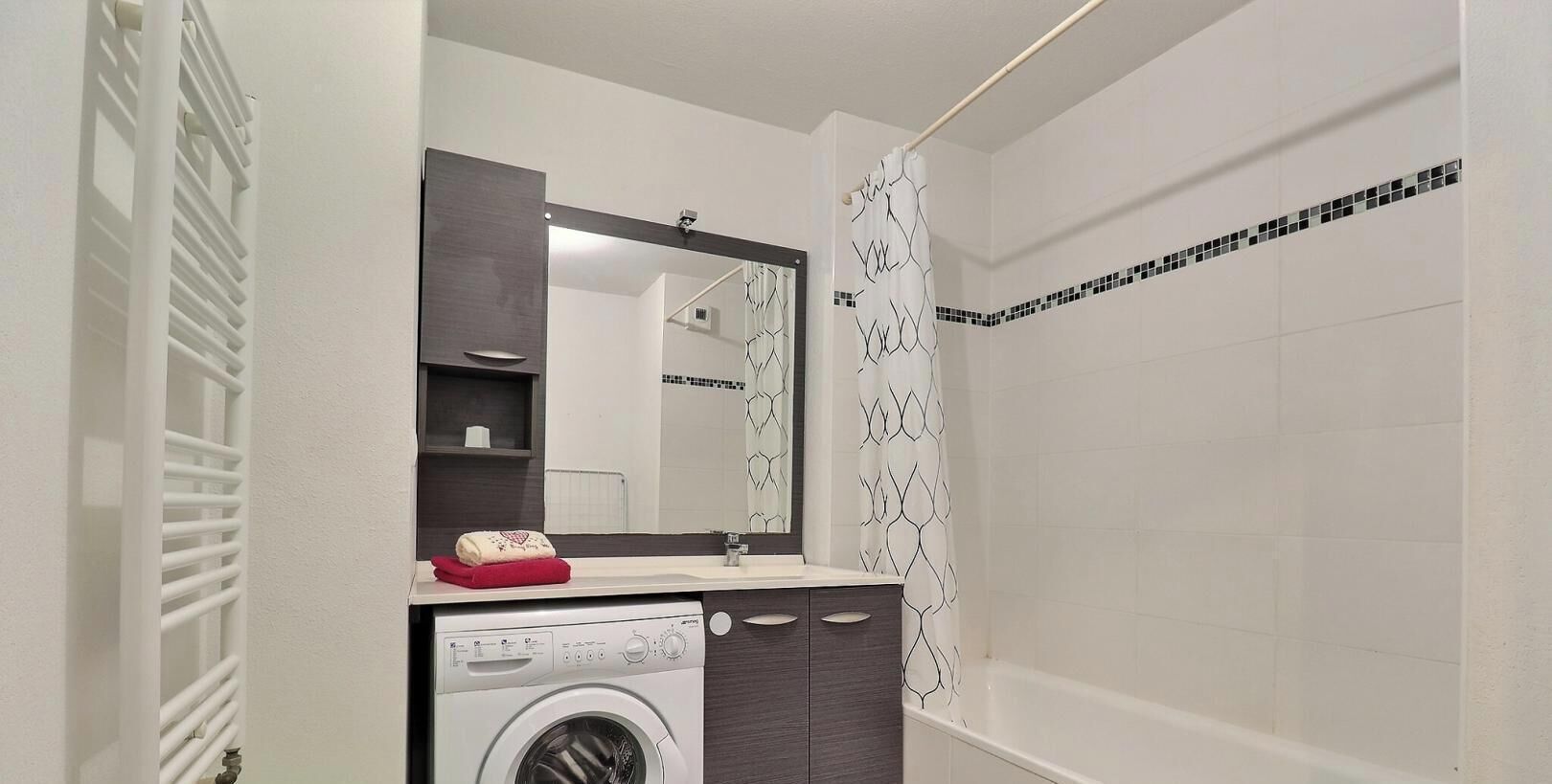 Un baño con lavadora, espejo, cortina de ducha y pared de azulejos.
