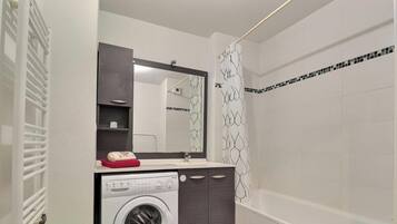 Un baño con lavadora, espejo, cortina de ducha y pared de azulejos.
