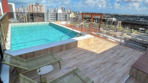 A rooftop pool with clear blue water, surrounded by wooden decking and metal railings. - Melhores Flats - Linda vista (João Pessoa)