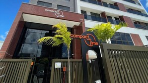 A tall building with a sign reading "compact time" at the entrance. - Melhores Flats - Linda vista (João Pessoa)