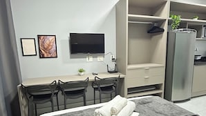 A hotel room with a bed, a desk with chairs, a TV, a wardrobe, and an air conditioner. - Melhores Flats - Linda vista (João Pessoa)