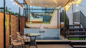 Ein moderner Außenbereich mit Whirlpool, umgeben von Glas, einer Holzterrasse, Korbstühlen und einer Treppe.