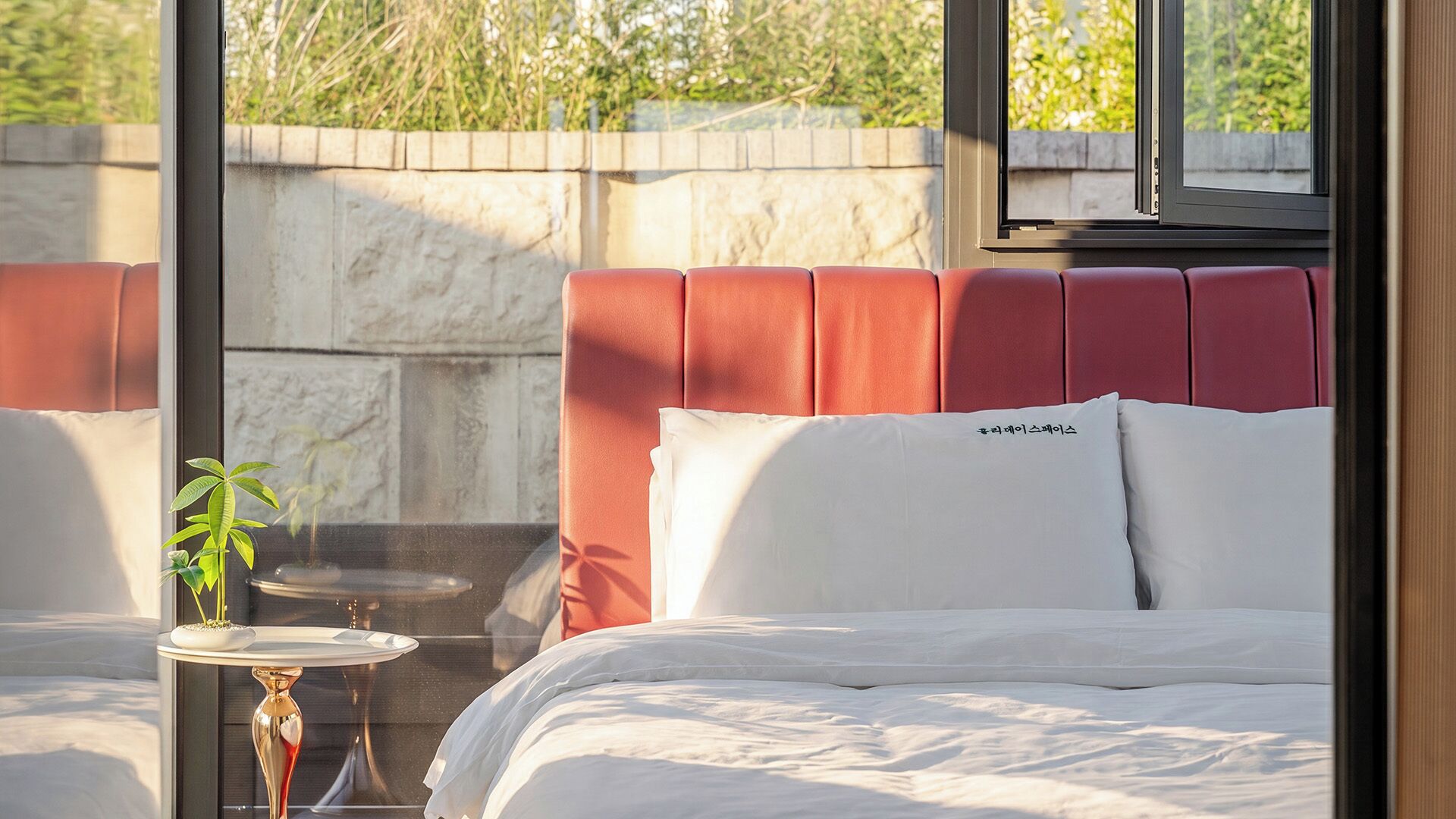 Une chambre d’hôtel avec un lit, une petite table ornée d’une plante et une vue sur la verdure environnante.