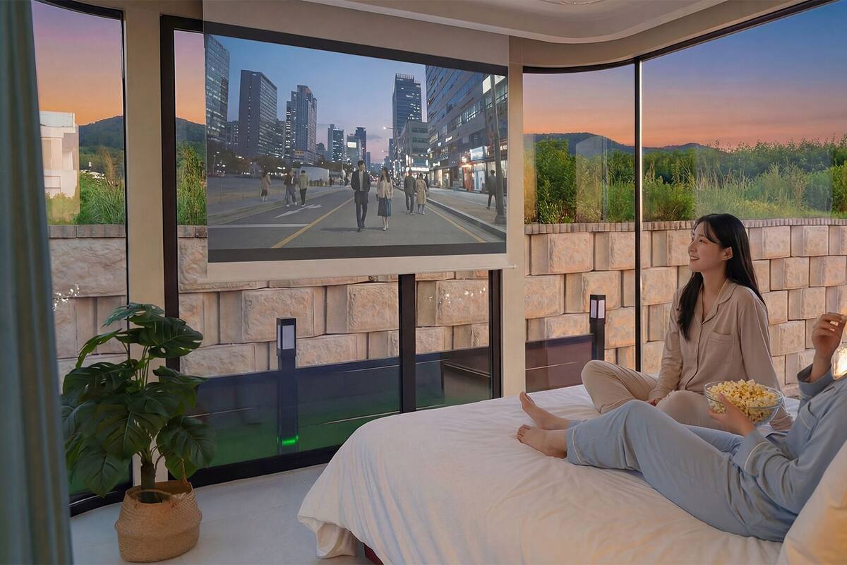 A bedroom with a large window, a bed, a potted plant, and a television screen displaying a cityscape.