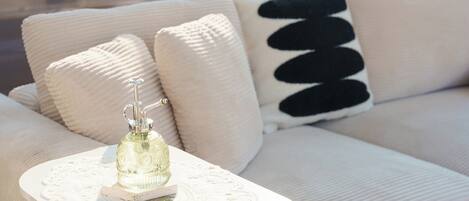 Un sofá blanco con un cojín texturizado, una mesa blanca con un mantelillo de encaje y una botella decorativa.