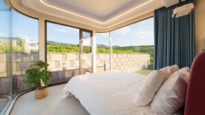 A bedroom with a large bed, a potted plant, and a view of a vineyard through large windows. - Gyeongju Holiday Space Pension (Gyeongju)