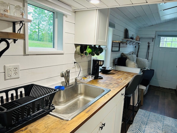 A kitchen with a stainless steel sink, wooden countertop, and a window with a view of greenery.