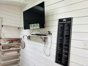 A room with a mounted television, a shelf with board games, and a wall-mounted list of movie quotes.