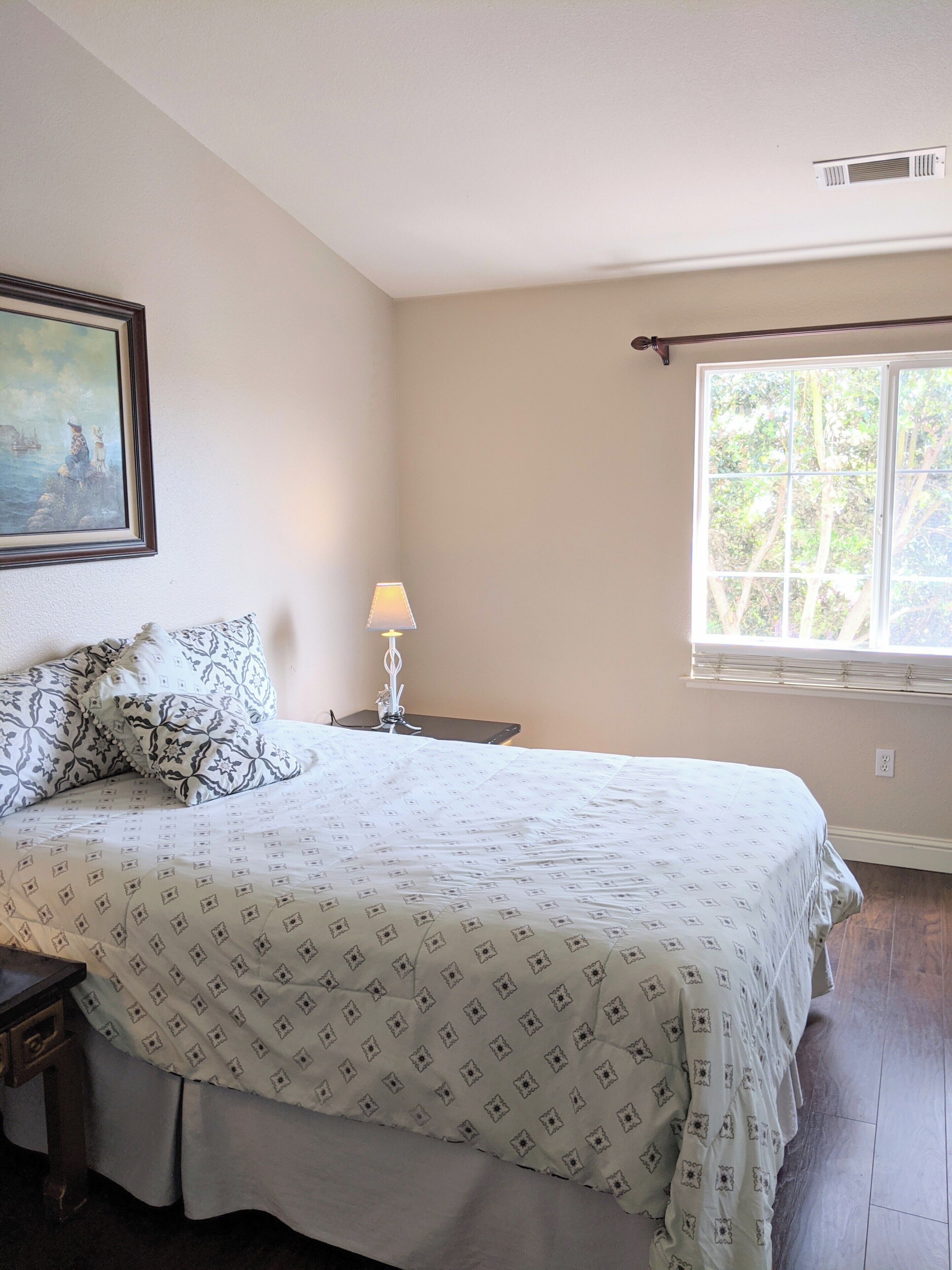 A bedroom with a bed, a nightstand, a lamp, a window with blinds, and a painting on the wall. - Executive home close to Keller Beach & Point Pinol shoreline extended stay (Richmond)