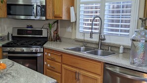 A kitchen with wooden cabinets, stainless steel appliances, a double sink, and a window with blinds. - Executive home close to Keller Beach & Point Pinol shoreline extended stay (Richmond)