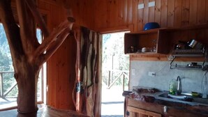 A rustic wooden interior with a large tree trunk, a wooden door, and a kitchen area with a sink and cabinets. - Secluded mountain cabin: steps to hot spring, river ,& lake (Futrono)