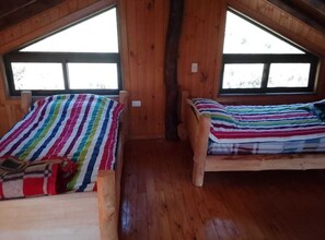 Due letti di legno con lenzuola a righe in una stanza con pareti di legno e ampie finestre.