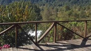 A wooden deck with a metal railing overlooking a mountainous landscape with dense forest and a visible valley. - Secluded mountain cabin: steps to hot spring, river ,& lake (Futrono)
