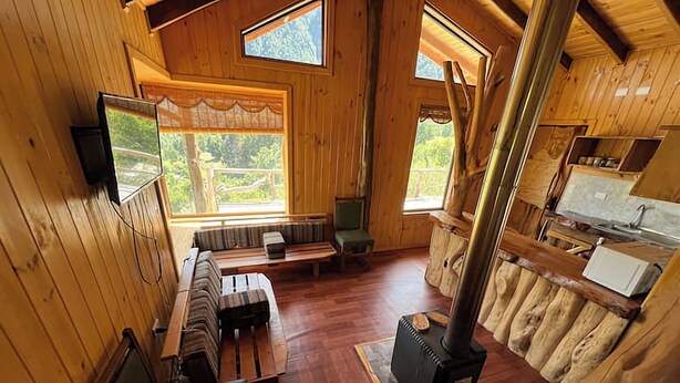 A cabin with wooden walls, a fireplace, a television, and a large window. - Secluded mountain cabin: steps to hot spring, river ,& lake (Futrono)