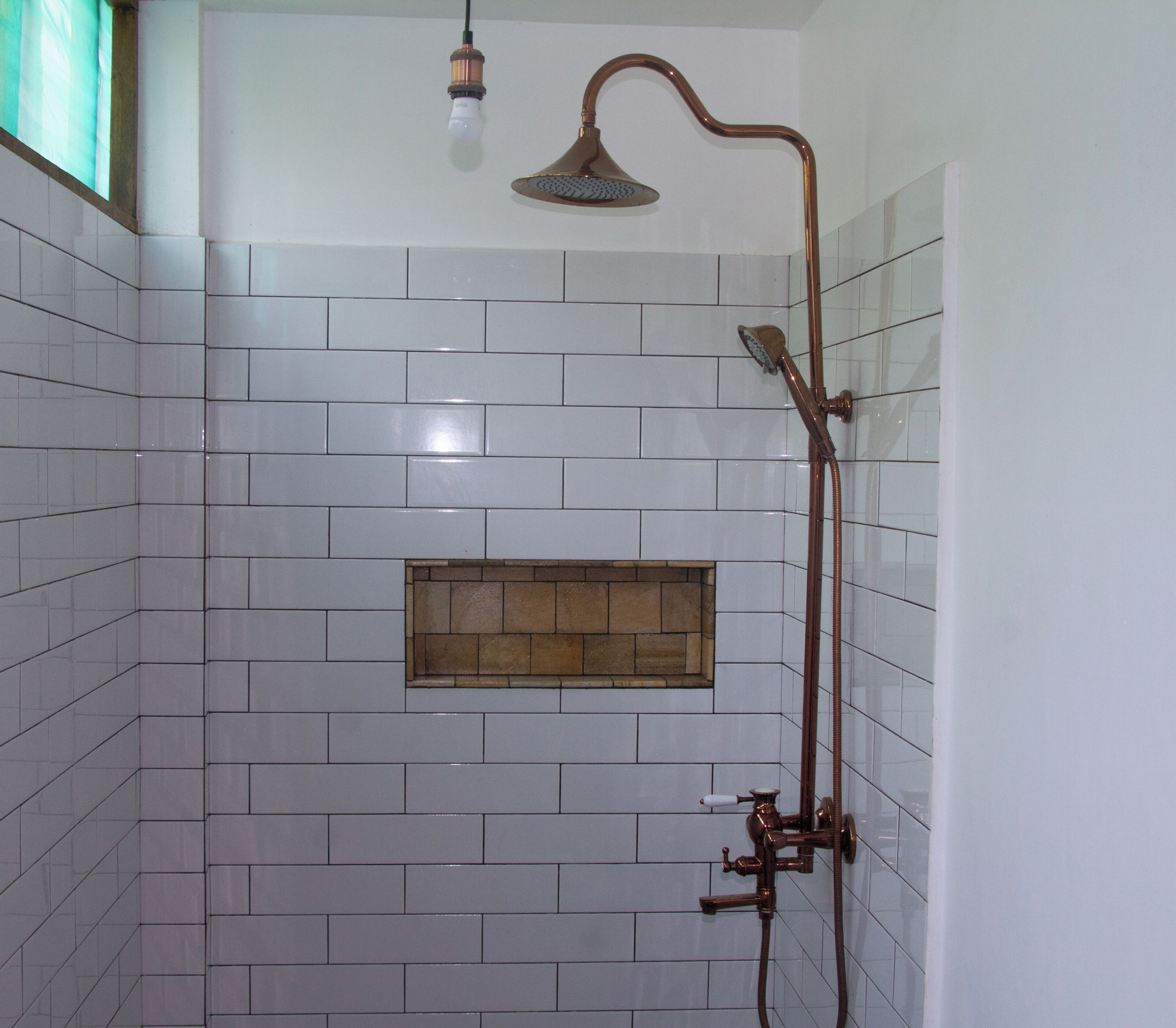 Ein Badezimmer mit weißen Fliesenwänden, einer Dusche mit Duschkopf und einer Leuchte.