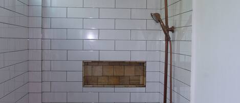 Un baño con paredes de azulejos blancos, una ducha con cabezal curvo e iluminación.