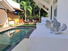 Un área junto a la piscina con una pared blanca, una escultura decorativa y una hamaca al fondo.