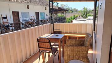 An outdoor seating area with a wooden table and wicker chairs, overlooking a residential area with houses and a clear sky.