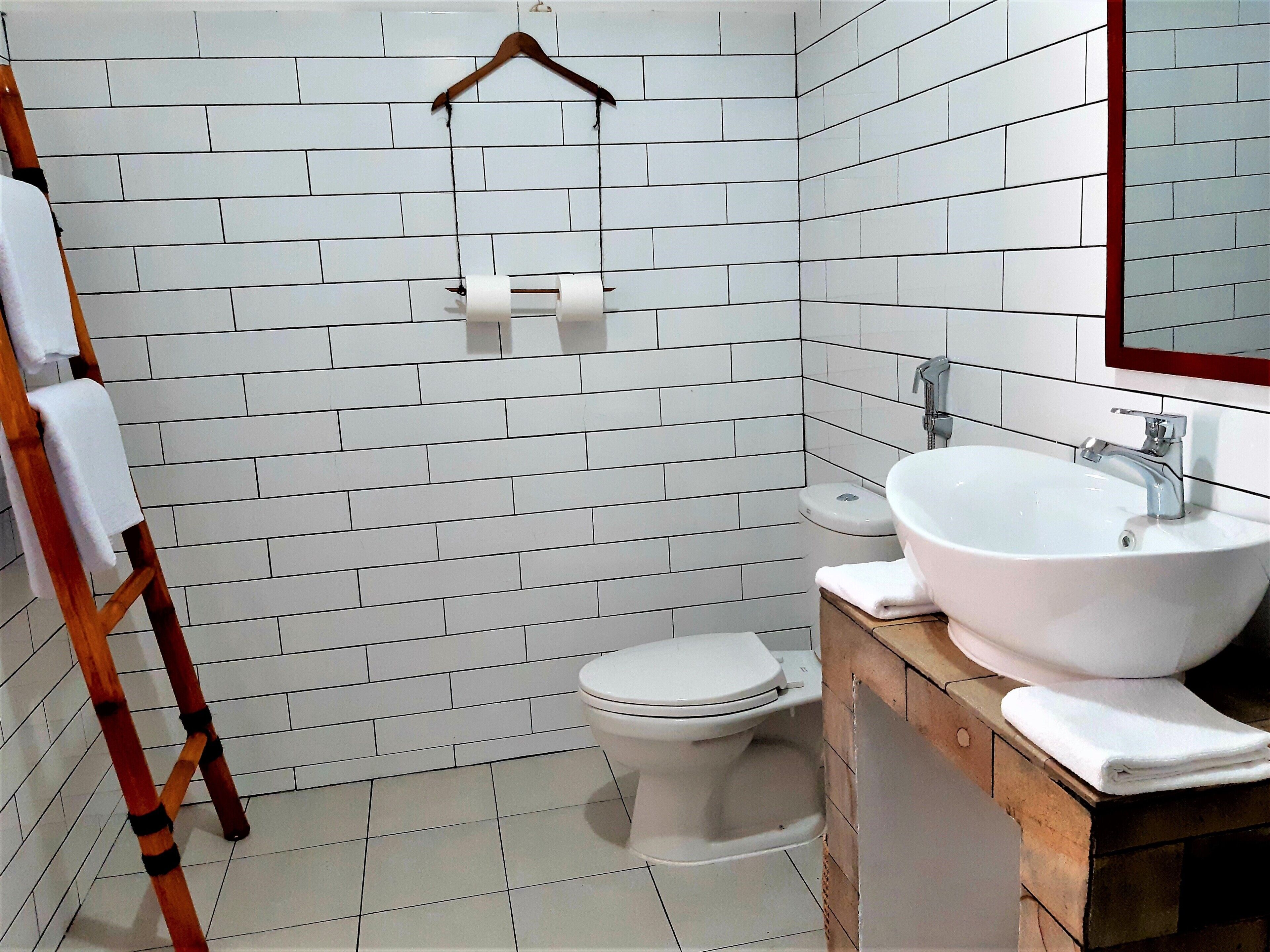 A bathroom with white subway tiles, a white toilet, a wooden vanity with a sink, and a wooden ladder.
