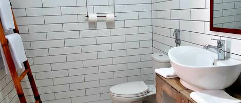 A bathroom with white subway tiles, a white toilet, a wooden vanity with a sink, and a wooden ladder.