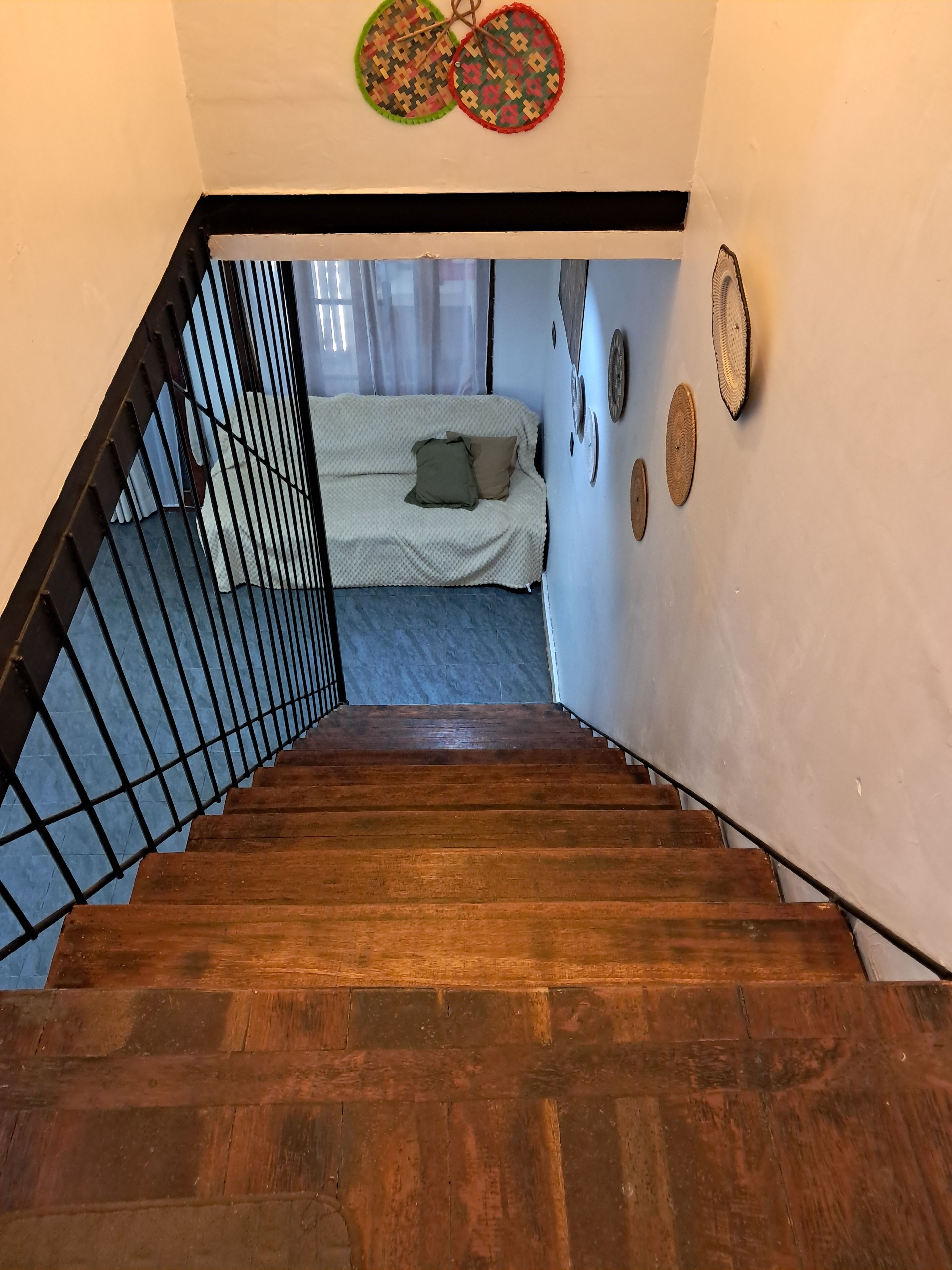 A wooden staircase leading to a room with a bed, a window with curtains, and wall decorations.