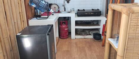 Een kleine keuken met een koelkast, gasfles en gasfornuis.